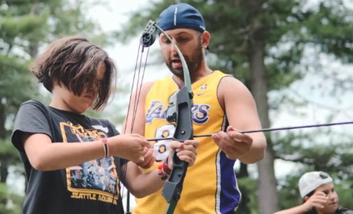 counselor teaching a camper how to shoot a bow and arrow