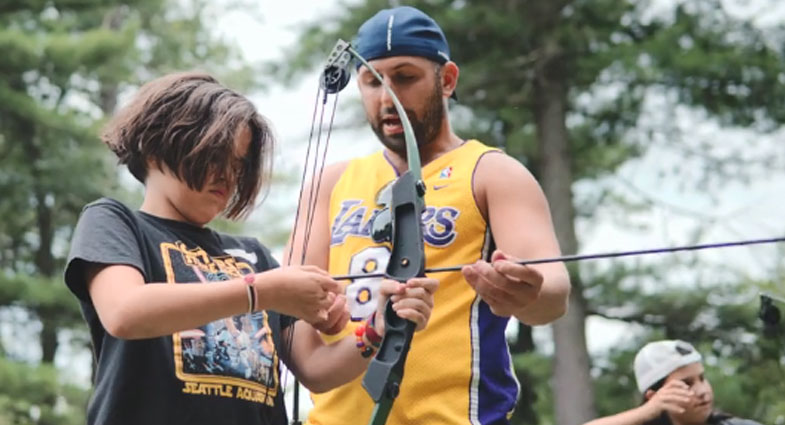 counselor teaching a camper how to shoot a bow and arrow