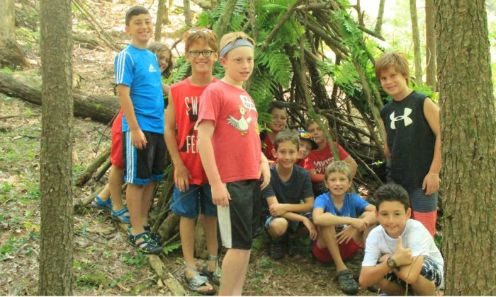 boys posing in front of the shelter they made in the woods