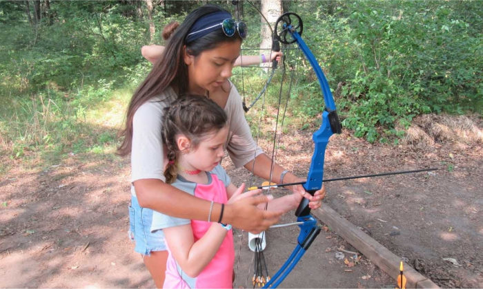 counselor helping a camper shoot a bow and arrow