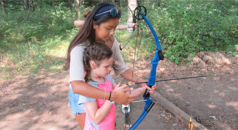 counselor helping a camper shoot a bow and arrow