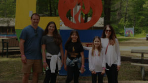 family poses in front of the Chi logo at camp