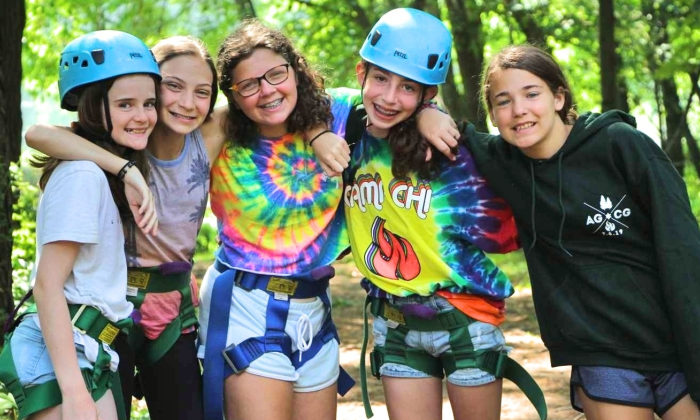 campers wearing climbing gear smiling for the camera before they climb the rock wall