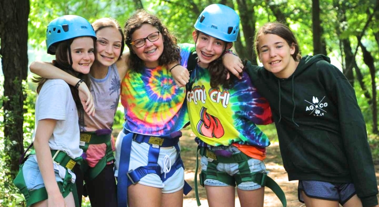 campers wearing climbing gear smiling for the camera before they climb the rock wall
