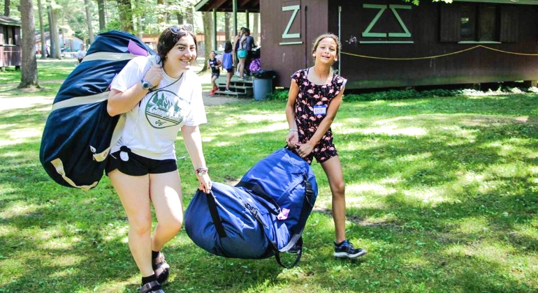 counselor helps her camper move her duffles to the cabin