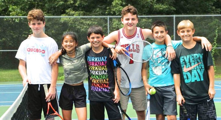 campers with tennis rackets smiling for the camera on the tennis court
