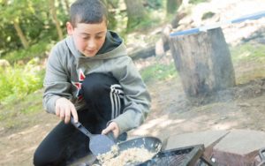 boy cooking outdoors over a fire