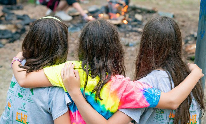 three girls with their arms around each other looking at the camp fire